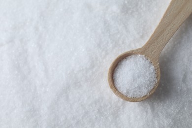 Photo of Wooden spoon on white sea salt, top view. Space for text