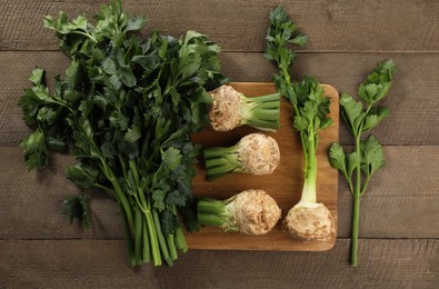 Photo of Fresh raw celery roots and stalks with leaves on wooden table, flat lay