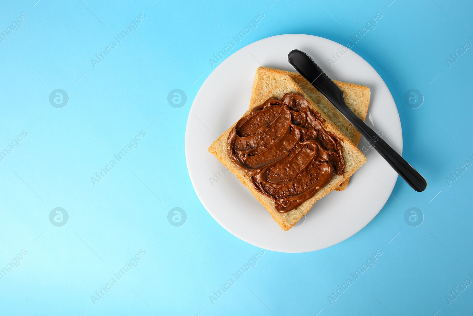 Photo of Tasty toast with chocolate paste on light blue background, top view. Space for text