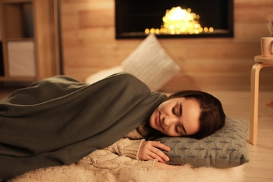 Photo of Young woman sleeping near decorative fireplace at home. Winter season