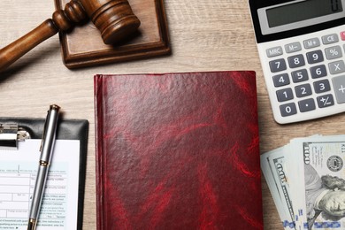 Photo of Tax law. Book, calculator, gavel, dollar banknotes and form on wooden table, flat lay