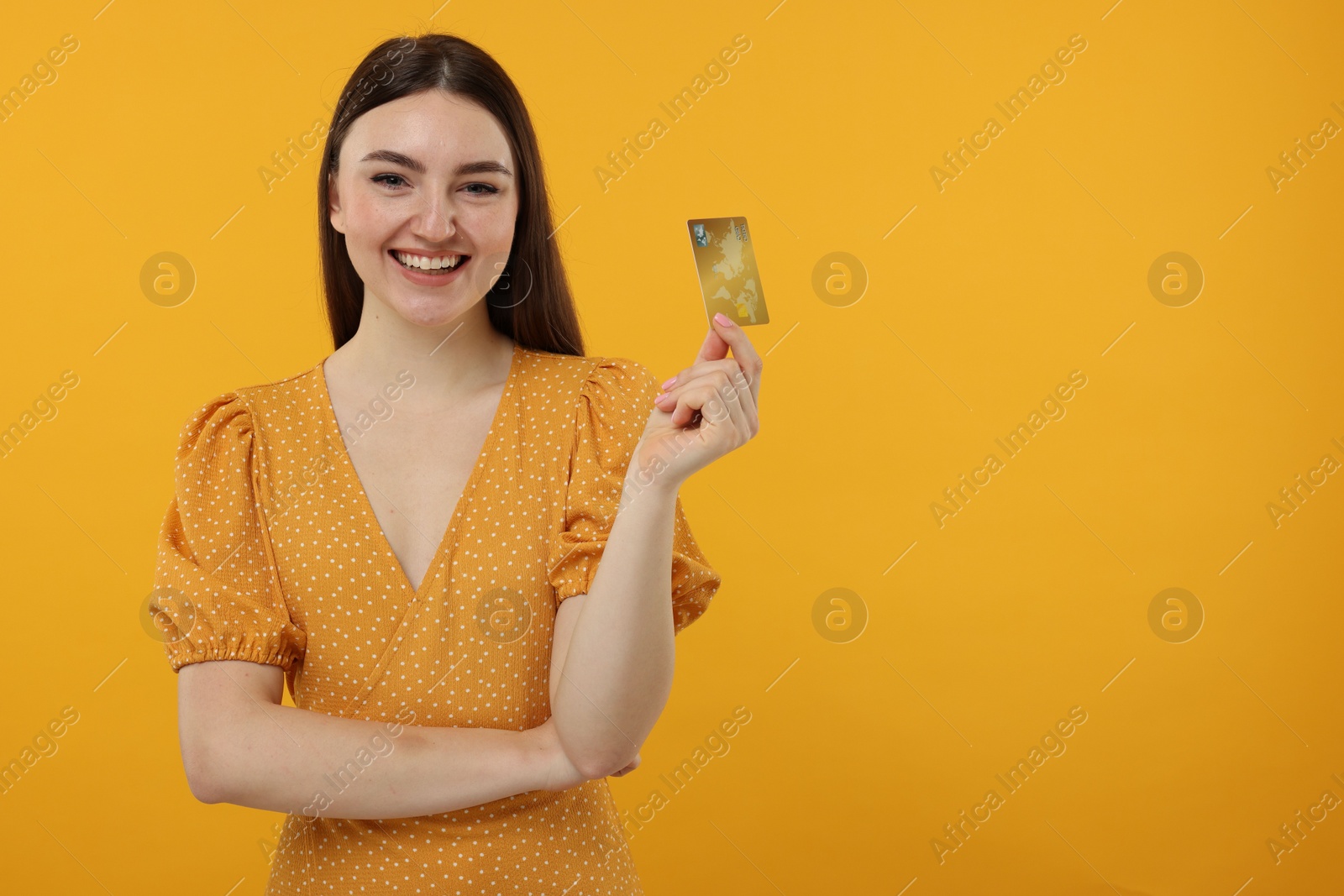 Photo of Happy woman with credit card on orange background, space for text