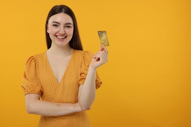 Photo of Happy woman with credit card on orange background, space for text