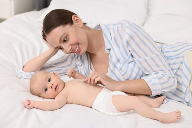 Happy young woman applying body cream onto baby`s skin on bed