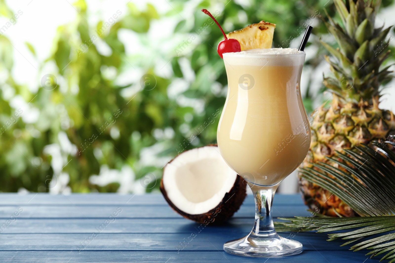 Photo of Tasty Pina Colada cocktail and ingredients on light blue wooden table, space for text