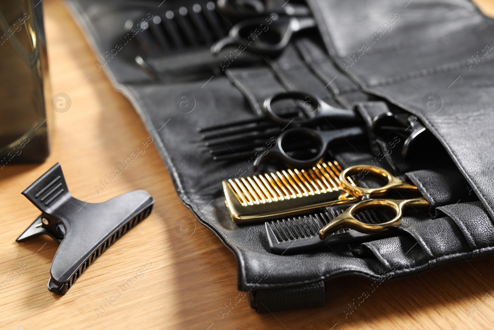 Photo of Hairdresser tools. Professional scissors and combs in leather organizer on wooden table, closeup