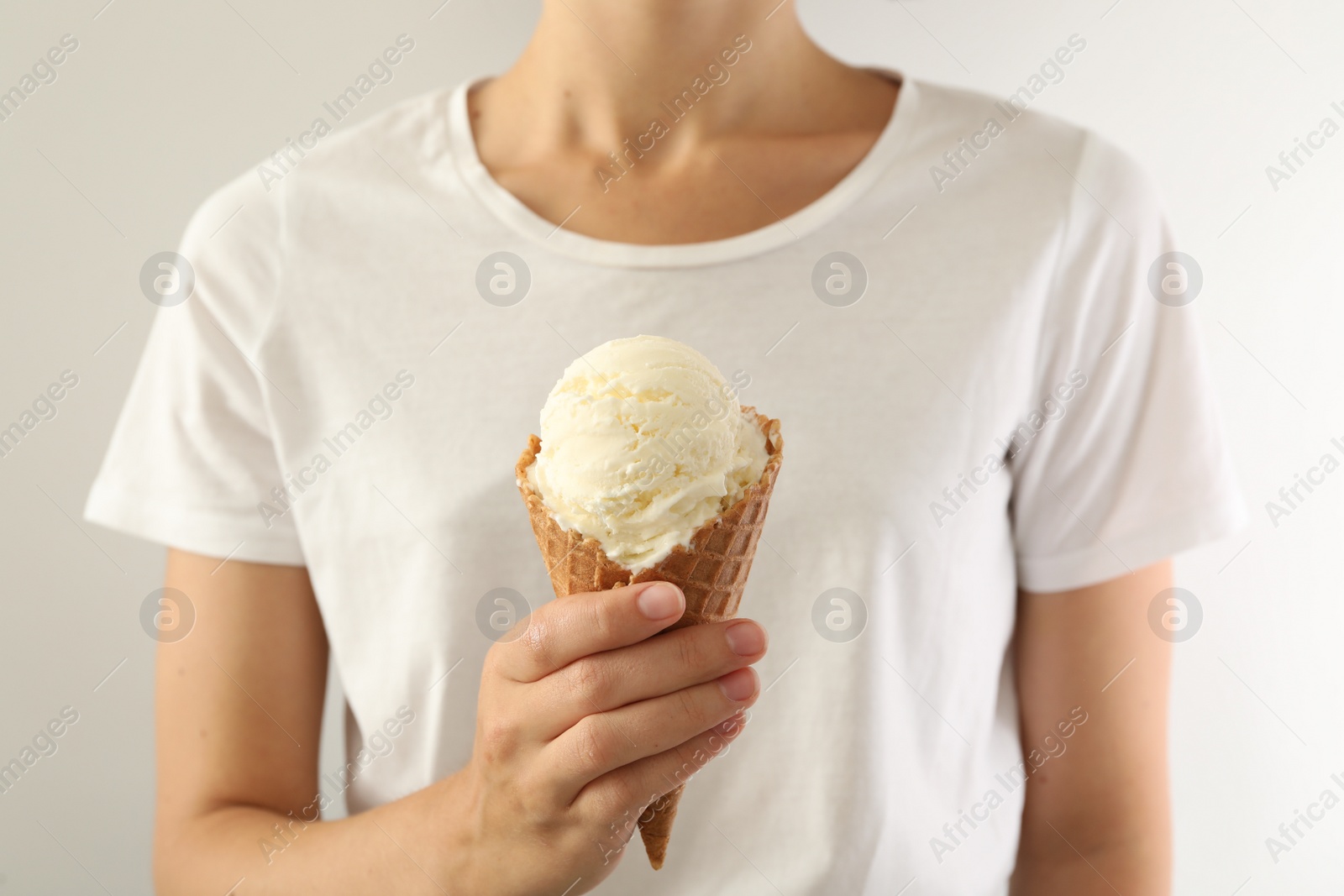 Photo of Woman holding ice cream in wafer cone on light background, closeup