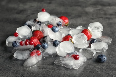 Photo of Different frozen berries and ice cubes on gray table