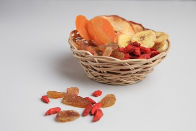 Wicker basket with different dried fruits on white background