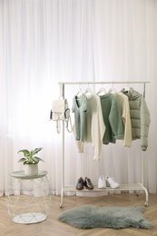 Rack with stylish warm clothes and shoes in modern dressing room