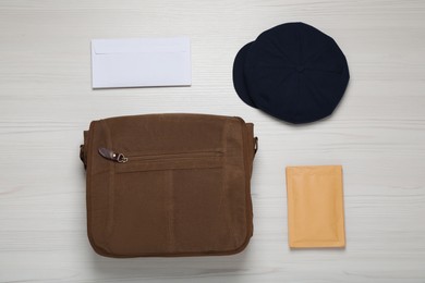Postman hat, bag and mails on white wooden table, flat lay