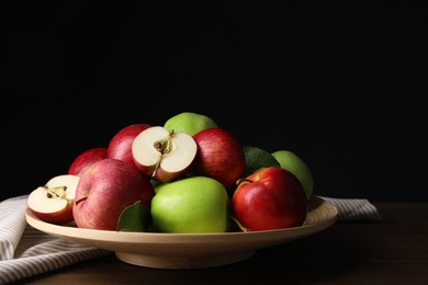 Photo of Plate with fresh ripe apples and leaves on wooden table against dark background