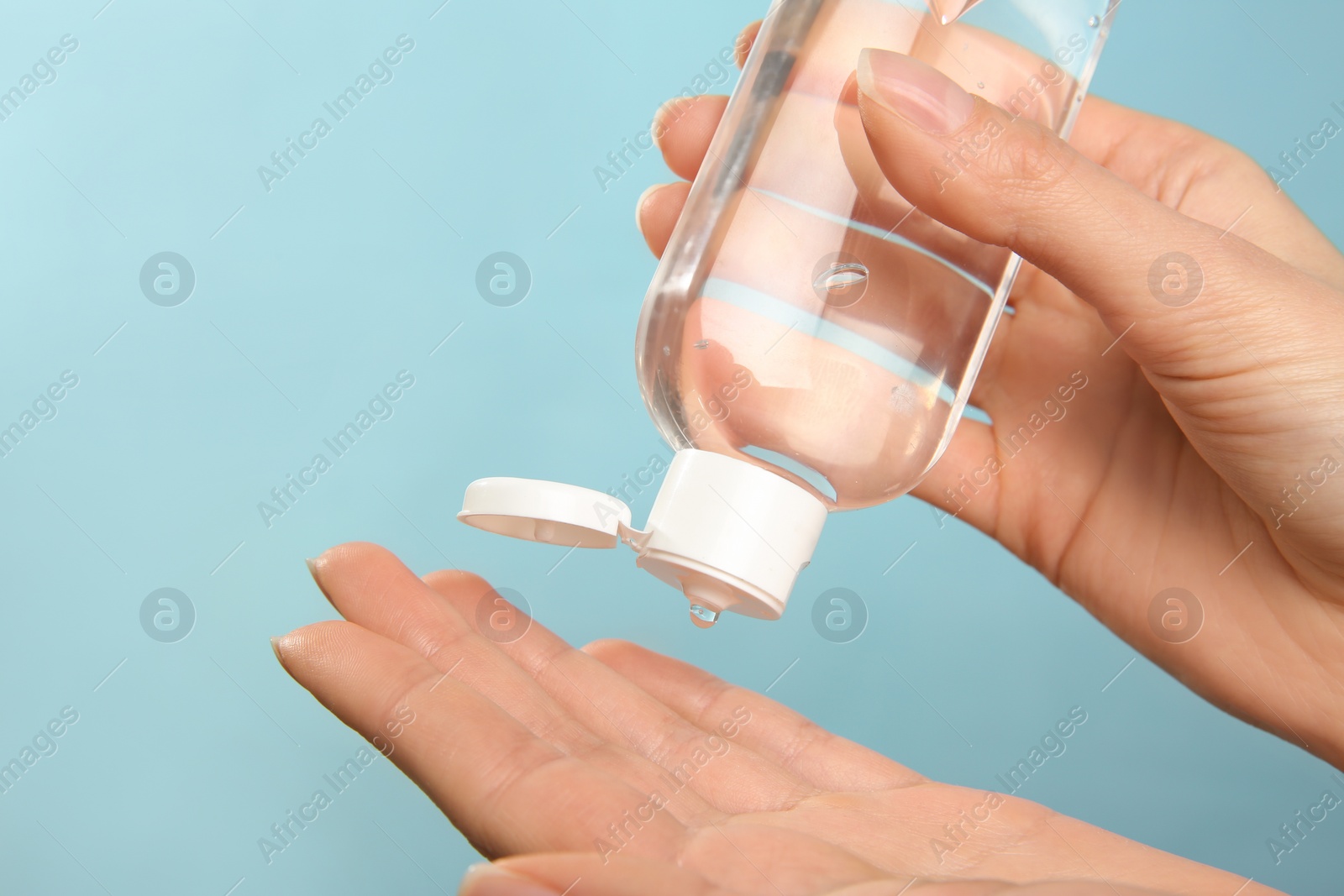 Photo of Woman applying antiseptic gel on light blue background, closeup