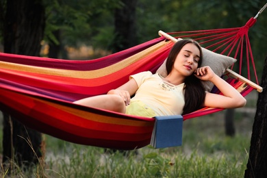 Young woman with book resting in comfortable hammock at green garden