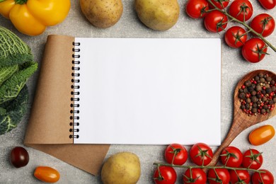 Recipe book surrounded by different fresh vegetables on grey table, flat lay with space for text. Cooking classes