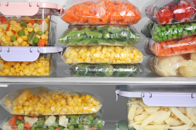 Photo of Plastic bags and containers with different frozen vegetables in refrigerator