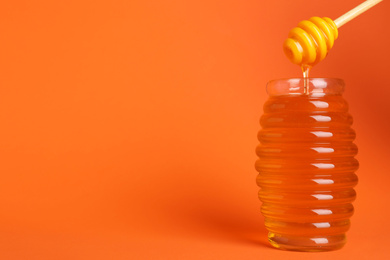 Photo of Jar of organic honey and dipper on orange background. Space for text
