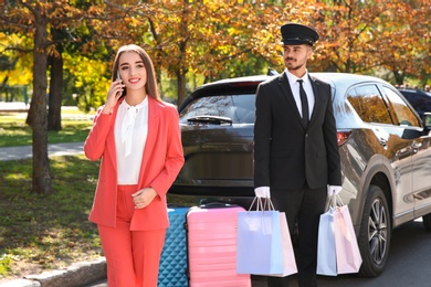 Handsome driver with shopping bags and young businesswoman near car outdoors