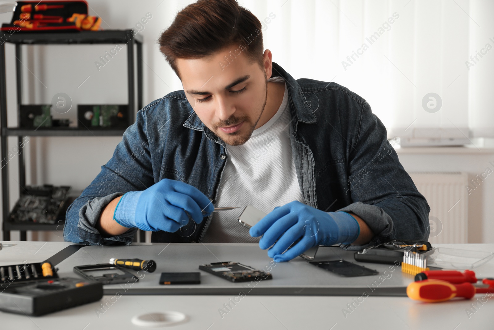 Photo of Technician repairing broken smartphone at table in workshop