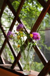 Photo of Bouquet of beautiful wildflowers in glass vase on wooden windowsill