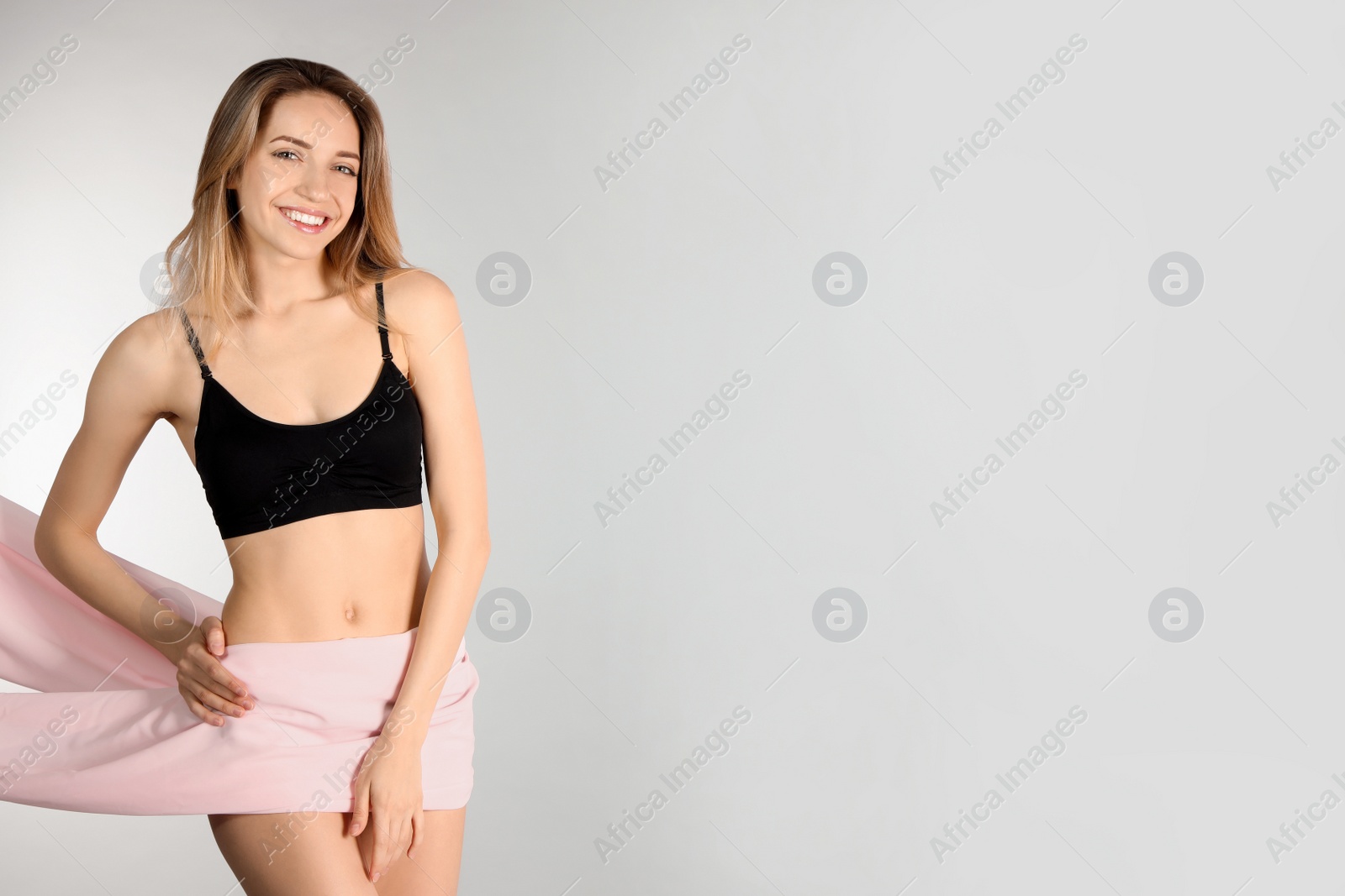 Photo of Young slim woman covering her body with fabric on light background. Space for text