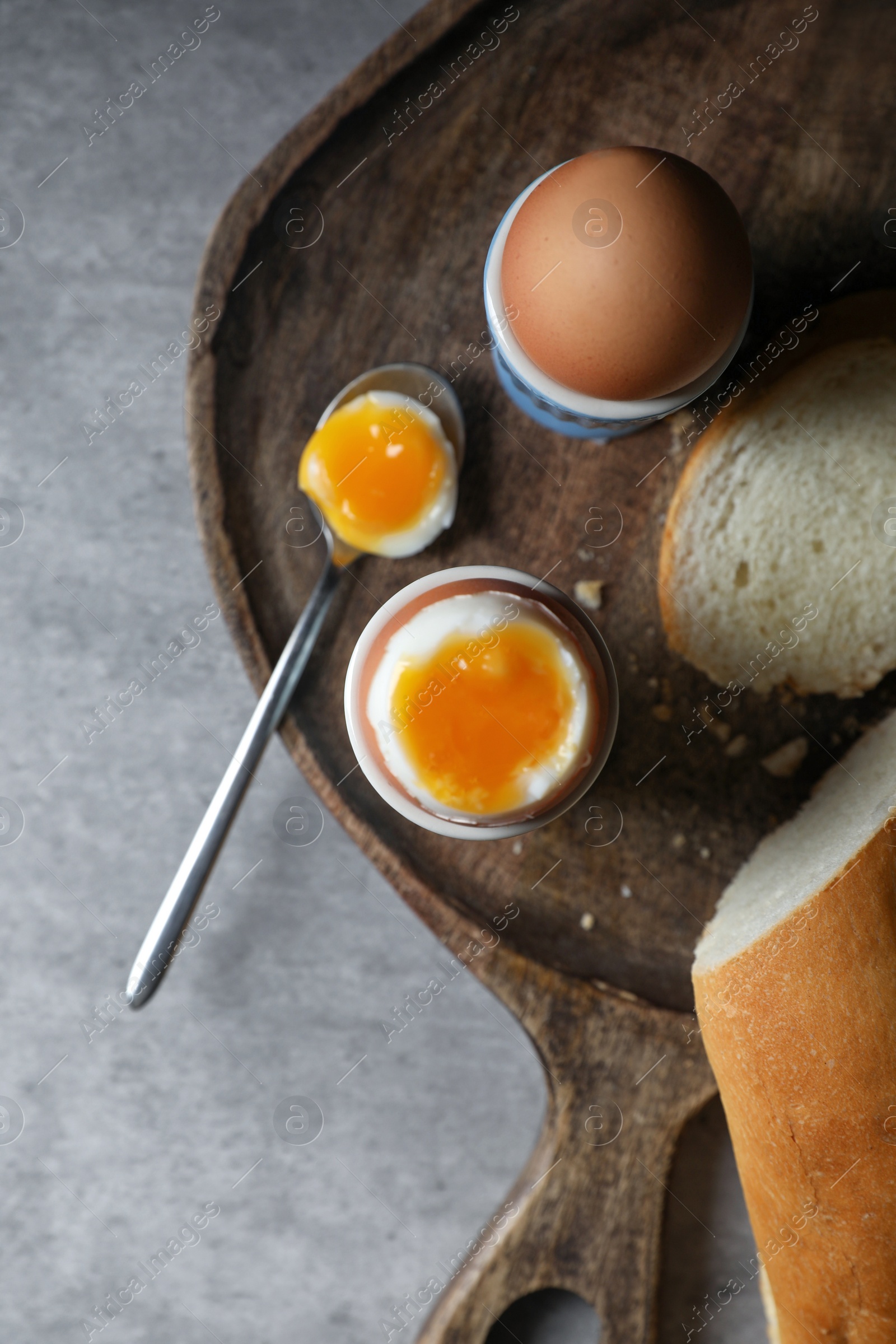 Photo of Fresh soft boiled eggs in cups and bread on grey table, flat lay