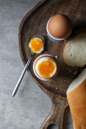 Fresh soft boiled eggs in cups and bread on grey table, flat lay