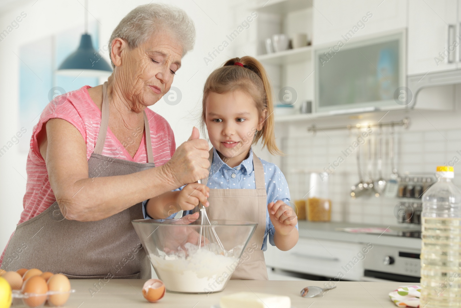 Photo of Cute girl and her grandmother cooking in kitchen