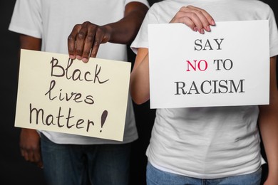 Photo of Young woman and African American man holding signs on black background, closeup. Racism concept