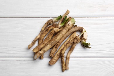 Photo of Cut horseradish roots on white wooden table, flat lay
