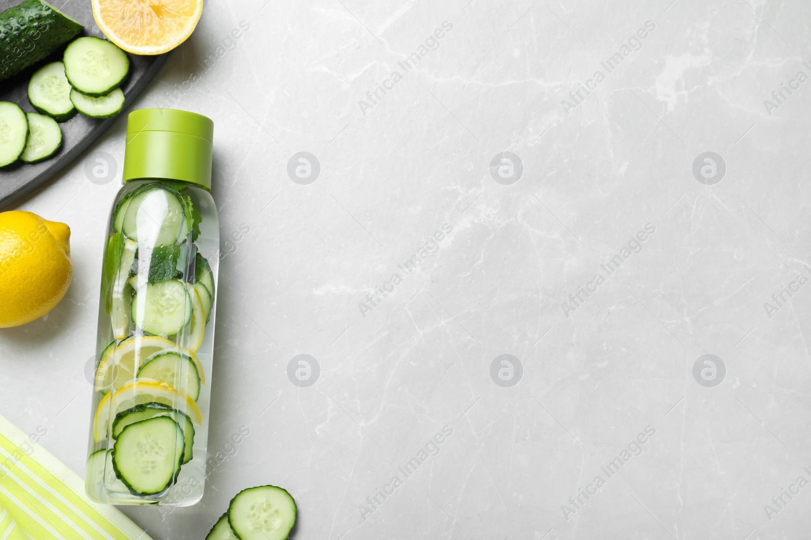Photo of Bottle of refreshing water with cucumber, lemon and mint on light grey table, flat lay. Space for text