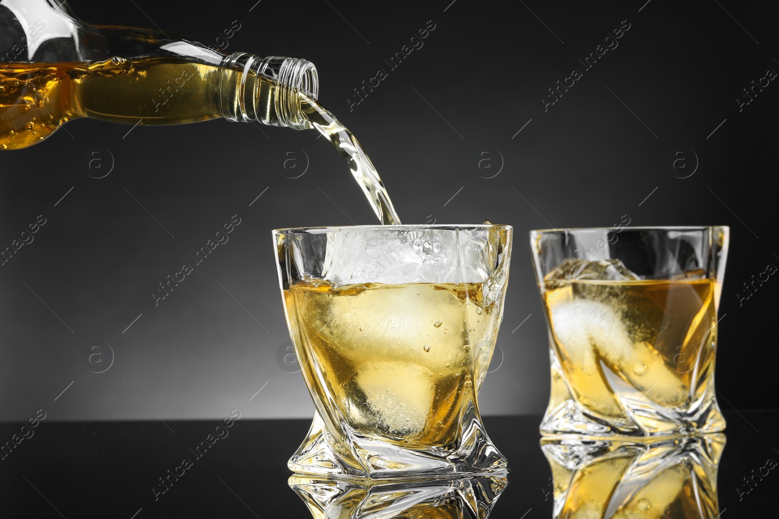 Photo of Pouring tasty whiskey from bottle into glass at mirror table, closeup