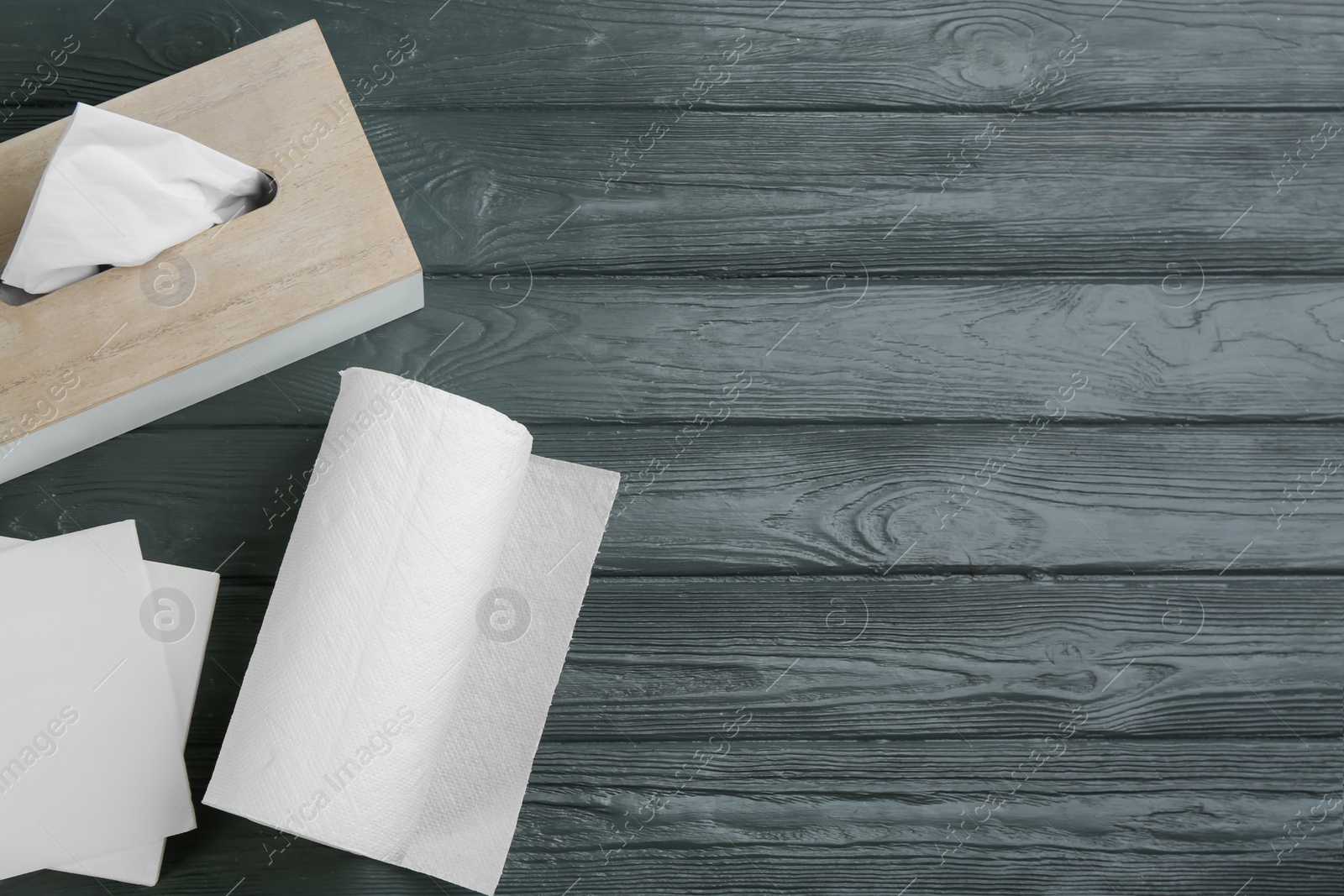 Photo of Clean napkins, box with tissues and roll of paper towels on grey wooden table, flat lay. Space for text