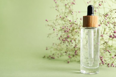 Photo of Bottle of face serum and beautiful flowers on light green background, closeup. Space for text