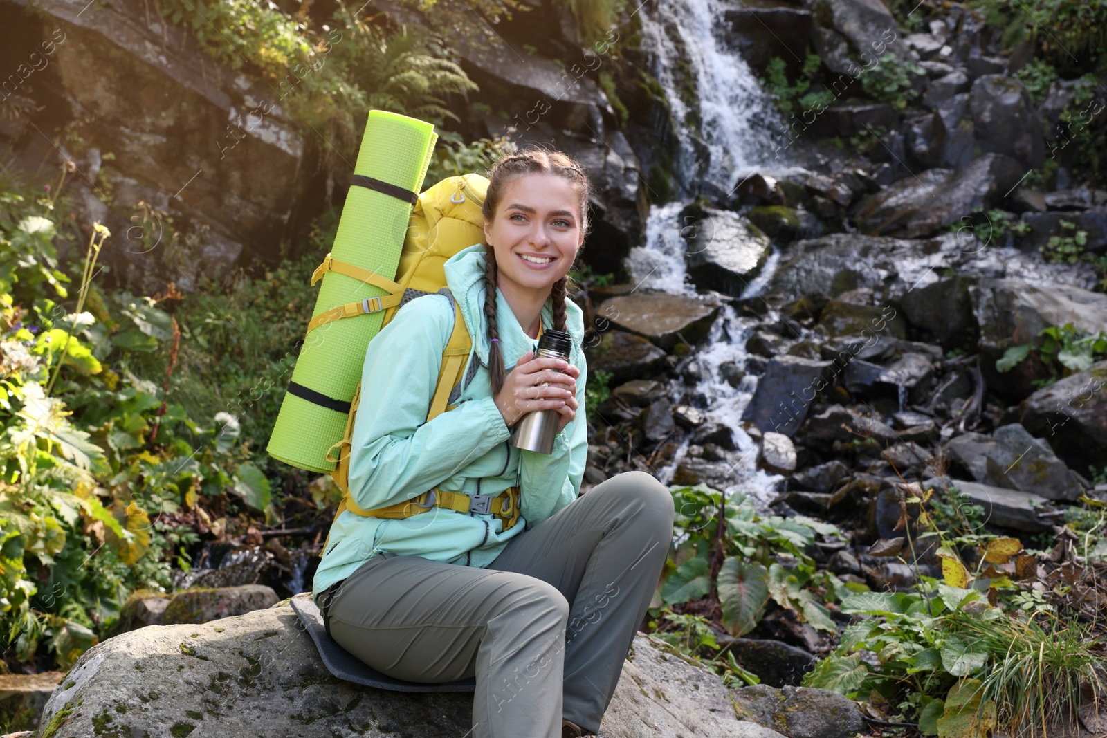 Photo of Tourist with vacuum flask near waterfall in mountains