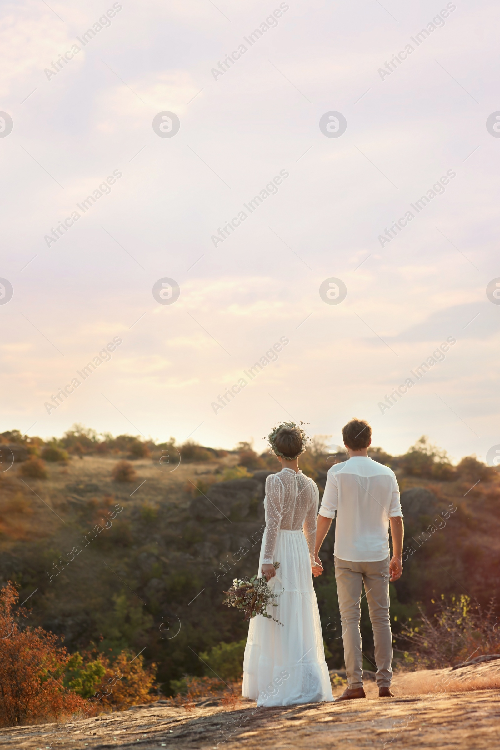 Photo of Happy newlyweds with beautiful field bouquet outdoors