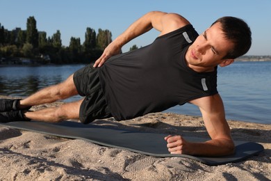 Photo of Sporty man doing side plank exercise on beach