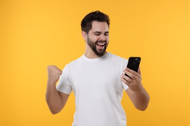 Photo of Happy young man using smartphone on yellow background