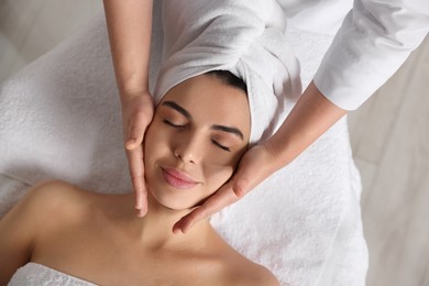 Photo of Beautiful woman receiving facial massage in beauty salon, closeup. Top view