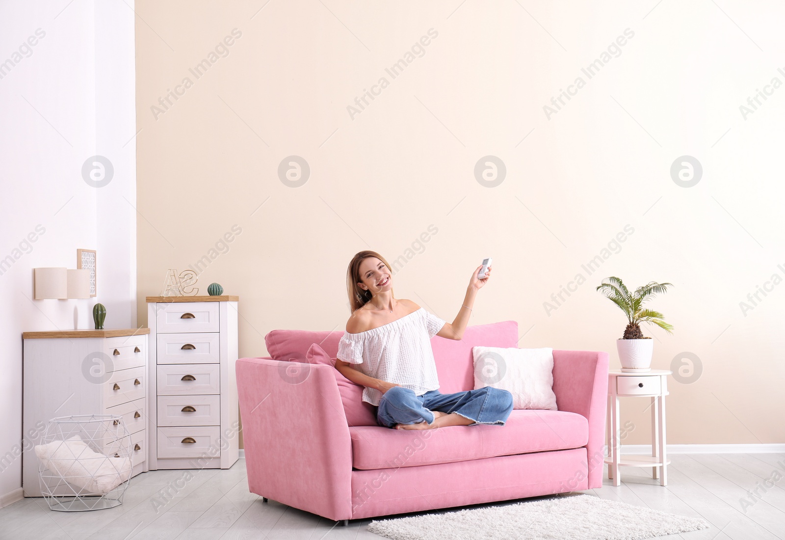 Photo of Happy young woman operating air conditioner with remote control at home