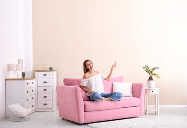 Photo of Happy young woman operating air conditioner with remote control at home