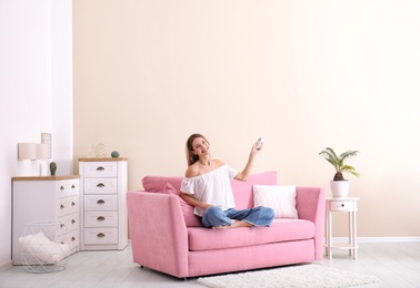 Happy young woman operating air conditioner with remote control at home