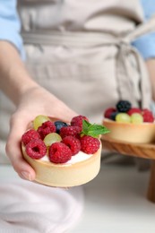 Photo of Woman with delicious tartlets at white table, closeup