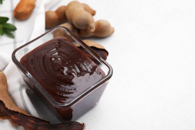 Photo of Bowl of tasty tamarind sauce and fresh pods on light table. Space for text