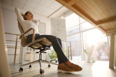 Photo of Young woman relaxing in office chair at workplace, low angle view