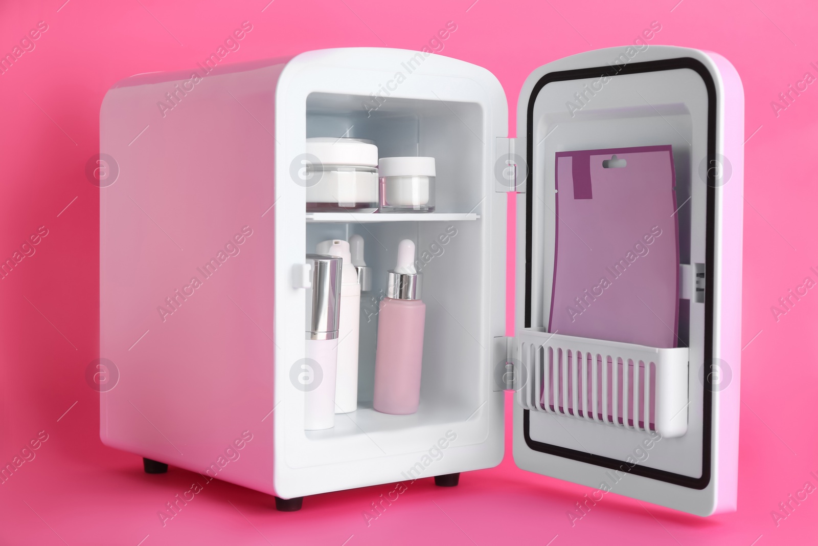 Photo of Open cosmetic refrigerator with skin care products on pink background