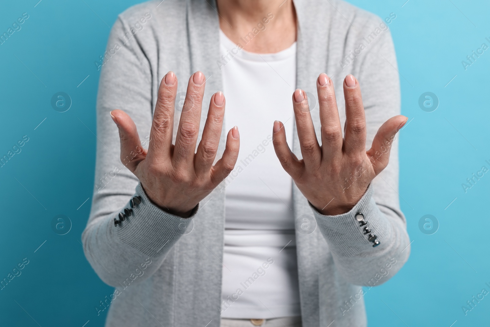 Photo of Arthritis symptoms. Woman suffering from pain in hands on light blue background, closeup