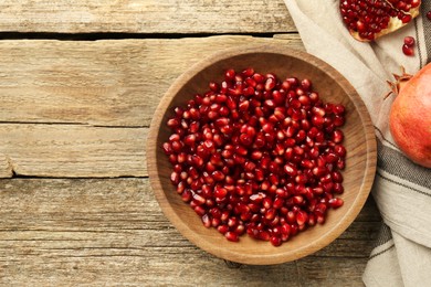 Photo of Ripe juicy pomegranate grains in bowl on wooden table, top view. Space for text