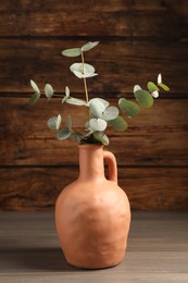 Photo of Beautiful eucalyptus branches in vase on wooden table indoors