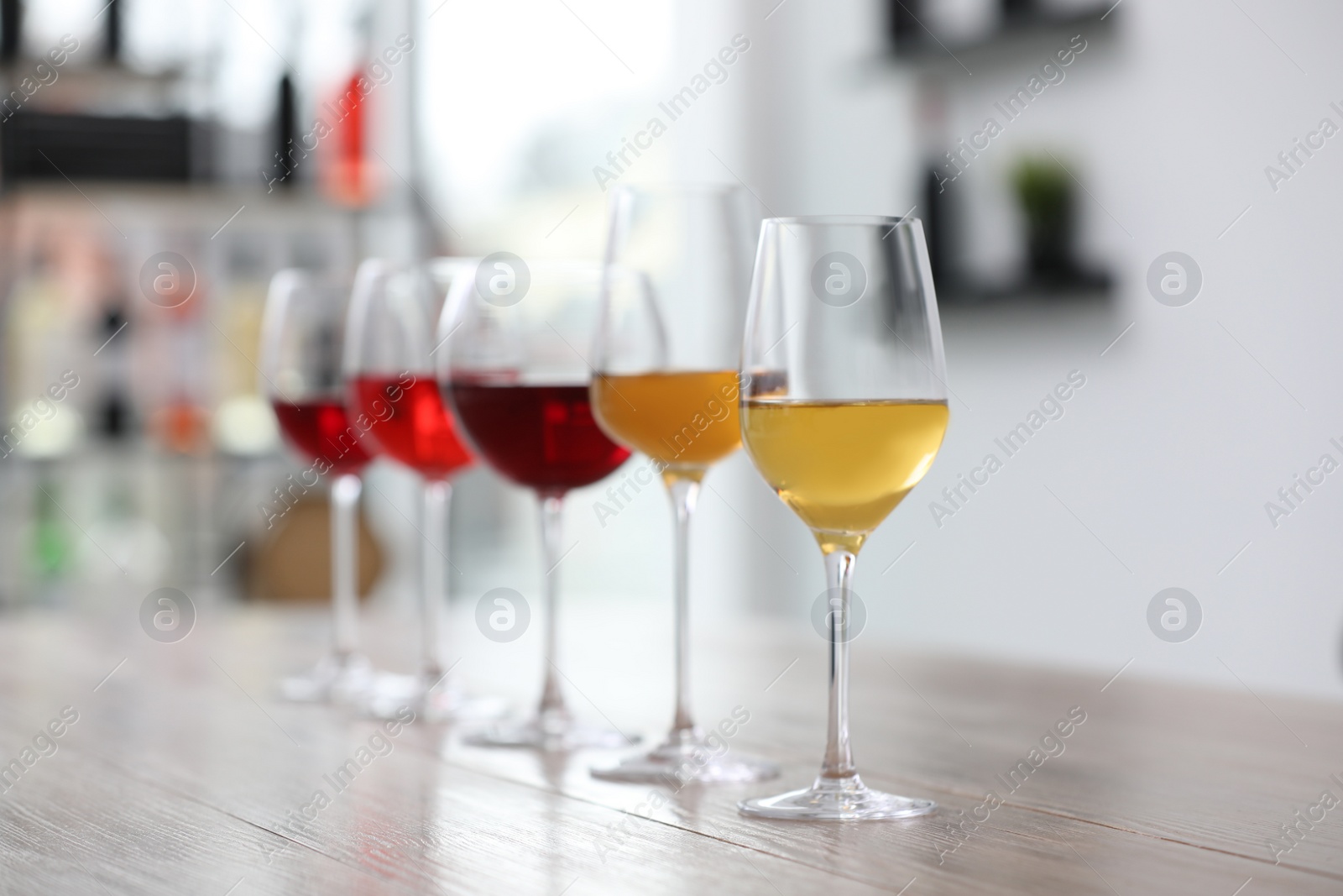 Photo of Different sorts of wine in glasses prepared for tasting on wooden table indoors